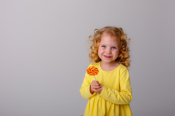 little curly blonde girl smiling holding a Lollipop hiding on a white background