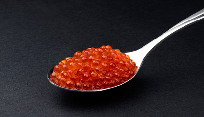 Red caviar in spoon isolated on black background