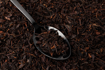 Dry tea leaves in black spoon over dark tea background