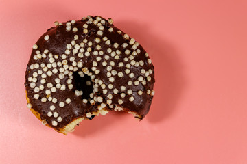 Bitten tasty chocolate donut on a pink background. Top view