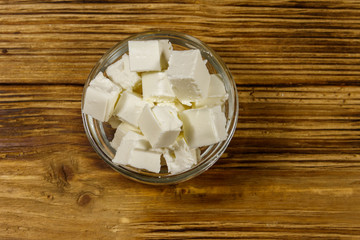 Feta cheese cubes in glass bowl on a wooden table. Top view