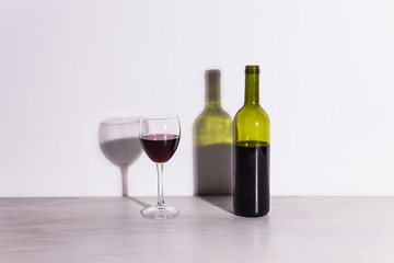 A glass of wine and a bottle casts a long shadow from the evening sun.