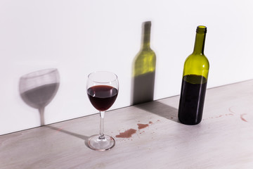 Bottle with wine and glass, red puddle of wine on the table. Cleaning after party concept.