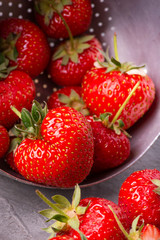 in the foreground, group of natural heart-shaped strawberries in an old colander