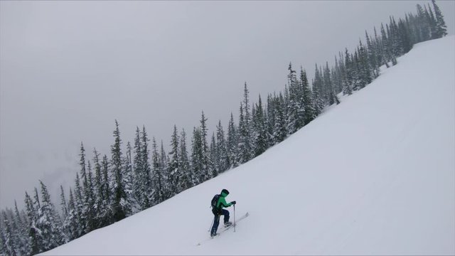 Dramatic Fly Over of Man Hiking Snowy Mountains in Winter Storm