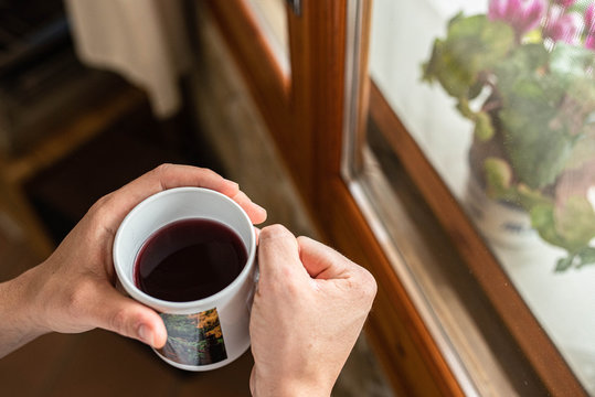 Close up overhead view of hands holding a cup of hot tea next to the window.