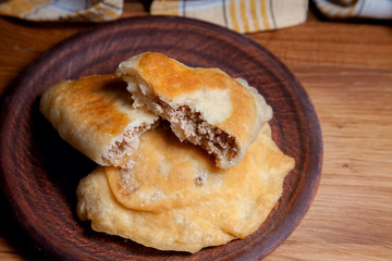 Clay plate of fried meat pies on wooden table.