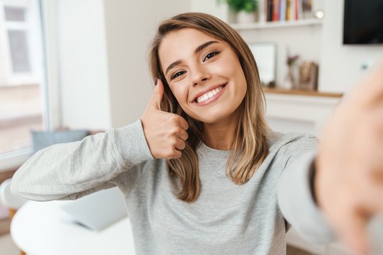Photo of young woman showing thumb up and smiling while taking selfie