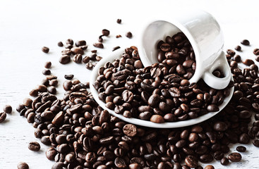 Coffee beans scattered from a coffee cup on a rough wooden background. Vintage photo.
