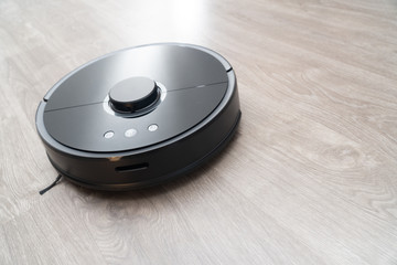 Robot vacuum cleaner black on the floor is cleaning, gray laminate