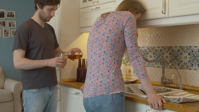 A tired woman in depression standing next to a sink in the kitchen. Alcoholic husband offers her a drink, she gives him a slap in the face. Home Conflict, Violence, and Harassment
