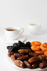 Dried fruits on a plate and cup of tea on a white background
