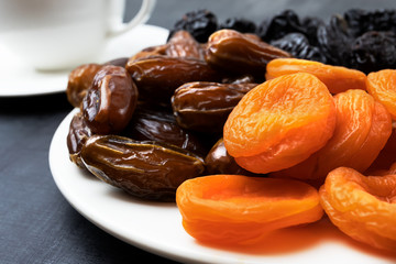 Dried fruits on a plate and cup of tea on a black background