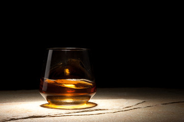 Half-full glass of whiskey is on a dark table