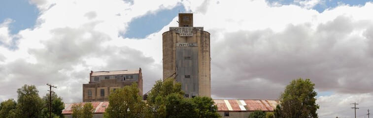 panorama of a large cement grain silo in a farming community rising high against a cloud filled blue sky, Nhill, rural Victoria, Australia