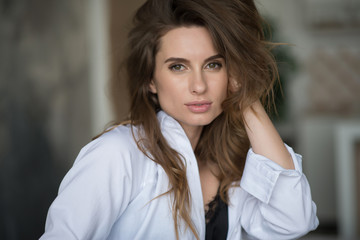 Beautiful elegant woman with flying hair and full lips in a white shirt on a gray background looks languidly at the camera. Beauty and fashionable style. Soft selective focus.