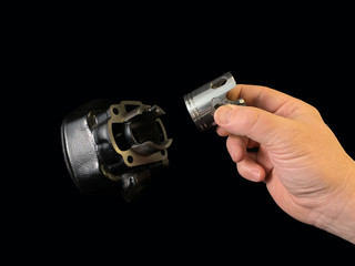 Cylinder and piston in a hand, on a black background. Piston system from a moped. Parts of a motor from a motorcycle, closeup.