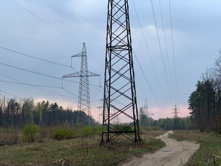 High voltage electric tower against a cloudy sky. High steel power pole, among the forest.