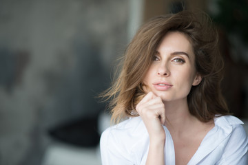 Beautiful elegant woman with flying hair and full lips in a white shirt on a gray background looks languidly at the camera. Beauty and fashionable style. Soft selective focus. © Tasha Sinchuk
