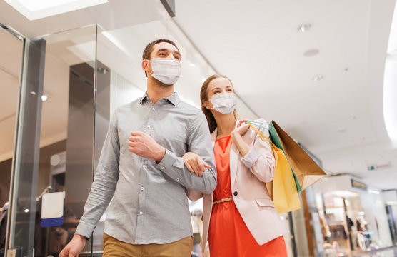 sale, consumerism and pandemic concept - happy young couple wearing face protective medical mask for protection from virus disease with shopping bags in mall
