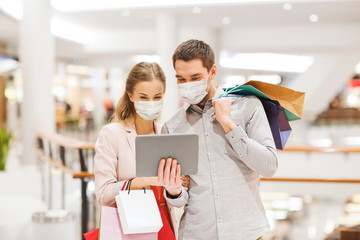 sale, technology and pandemic concept - happy young couple with shopping bags and tablet pc computer wearing face protective medical mask for protection from virus disease in mall
