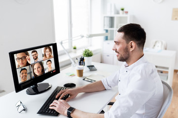 business, technology and online communication concept - happy businessman with computer having video call with partners at office