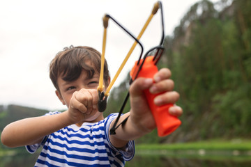 Young guy takes aim, preparing to make shot from slingshot. portrait boy is going to shoot on...