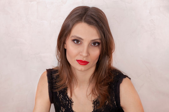 Close up portrait of young attractive woman with beautiful almond-shaped brown eyes and thick eyebrows, bright red lipstick and smoky make up. Oriental type of beauty, black dress, light background.