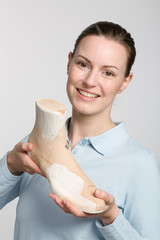 smiling female orthopedic shoemaker presents a handmade wooden last