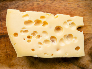 piece of yellow swiss cheese on wooden table close up
