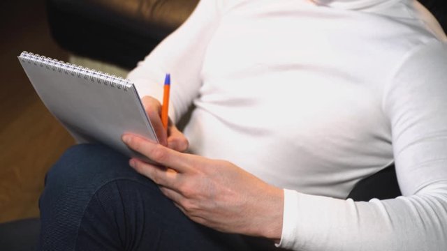 male hands in a white sweater closeup write with a ballpoint pen in a notebook text