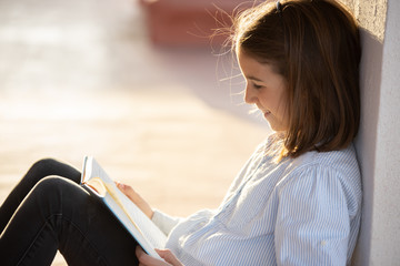 Smiling girl reading a book sitting on the rooftop
