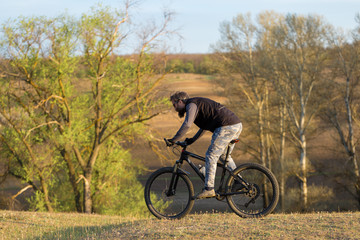 Fototapeta premium Sports brutal bearded guy on a modern mountain bike. Cyclist on the green hills in the spring.