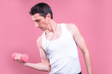 Side view of confident skinny young man hold one pink dumbbell in hand. Exercising hard. Alone in...