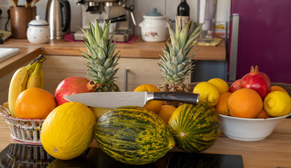 Many varieties of fresh and exotic fruits with a damascus kitchen knife standing on a cooking...