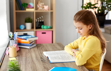 children, education and learning concept - little student girl reading book at home