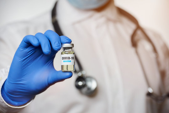 A male infectious disease physician wears a white coat and medical face mask holding in a hand in disposable medical glove a coronavirus vaccine. A doctor with a COVID-19 vaccine in a hospital. 