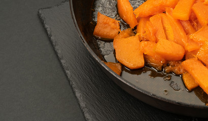Braised pumpkin with honey in a pan on a black background