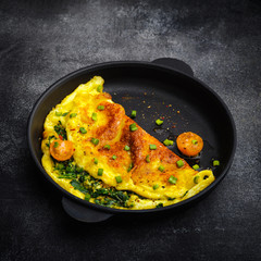 Omelet with spinach, green onions and cherry tomato in a black pan.