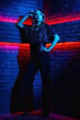 Beautiful girl model in neon lighting. Young woman in a dress with an open back in red with blue lighting in a club