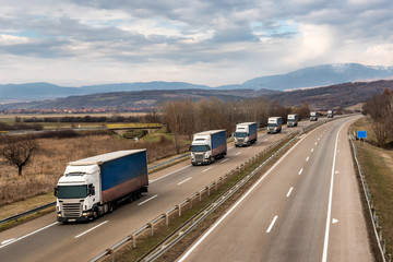 Convoy of transportation  trucks in line as a caravan or convoy on a country highway under an amazing blue sky