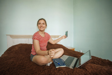 Fototapeta na wymiar Happy teenager talking on video on the mobile phone lying on a bed. Woman stay home and chatting online during the pandemic quarantine. Self isolation. Stay home. Work from home