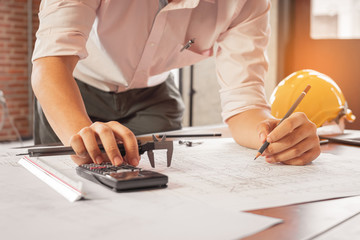 Engineer using calculator and sketching the drawing construction building. Civil engineering,...