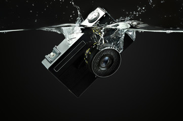 Retro camera drops into water, volumetric drops and splashes on black background. Underwater shooting.