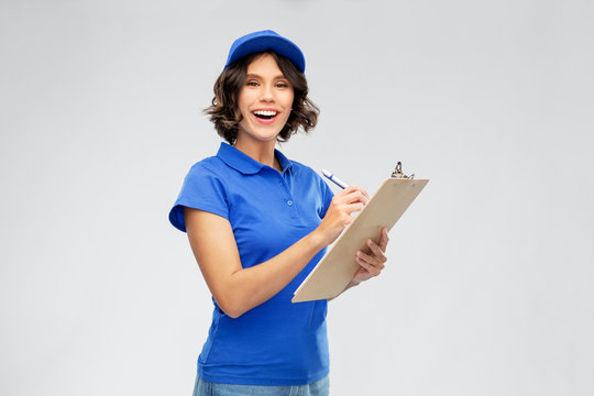 Mail Service And Shipment Concept - Happy Smiling Delivery Girl In Blue Uniform With Clipboard And Pen Writing Over Grey Background