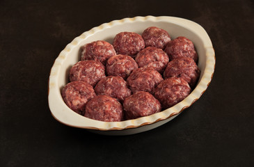 Juicy homemade beef patties in a ceramic baking dish are close-up ready for cooking on a dark background in the kitchen. Selective focus.