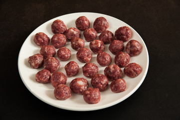 Juicy homemade beef meatballs on a white plate are close-up ready to cook on a dark background in the kitchen. Selective focus.