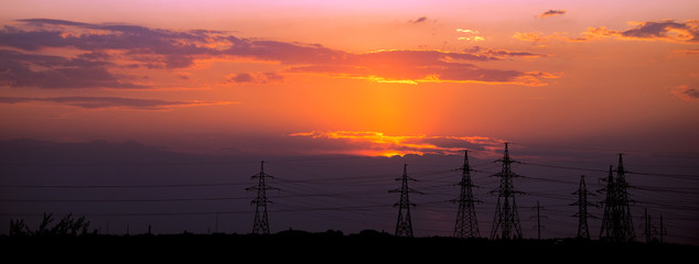 The setting sun on the background of a high-voltage station.Panorama of the high-voltage line.Field and aerial lines, silhouettes at dusk.Electric power industry and nature concept.