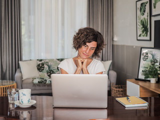 happy smiling remote online working woman talking with laptop, headset, notebook, mobile, pen and glass in casual outfit sitting on a work desk in her living room in her home office having video chat