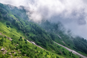 The green slopes of high mountains are hidden in clouds and fog. Melting snow in high mountains in...